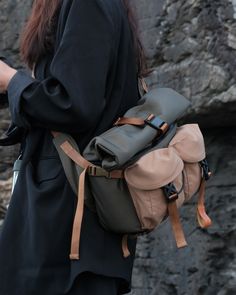 a woman with long hair wearing a hat and carrying a backpack on her back while standing in front of some rocks