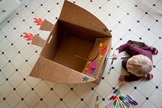 a young boy is playing with his cardboard box and crayons on the floor