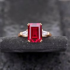 a red and white diamond ring sitting on top of a rock