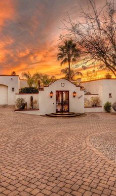 a white house sitting on top of a cobblestone road next to a palm tree