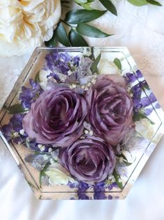 some purple flowers are in a glass vase on a white tablecloth and next to it is an artificial flower arrangement