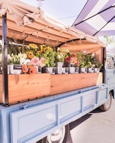 a blue truck is loaded with flowers and potted plants on the back, under an awning