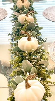 a long table with white pumpkins and greenery on the top, in front of a window