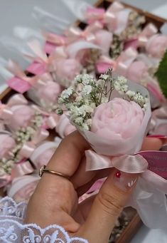 a hand holding a pink rose with white flowers on it next to a box of baby's breath