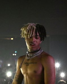 a man with dreadlocks standing in front of some lights and looking at his cell phone