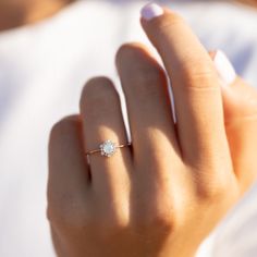 a woman's hand with a diamond ring on top of her finger and white nails