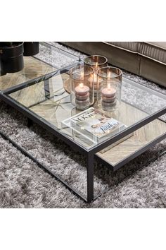 a glass coffee table with candles on it in front of a couch and grey carpet