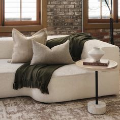 a white couch with pillows on it in front of a brick wall and window sill