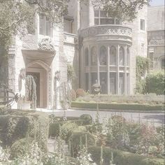 a large white house with lots of bushes and flowers in front of the entrance to it