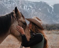 a woman in a cowboy hat kissing a horse