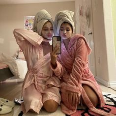 two women sitting on the floor in robes taking a selfie with their cell phone