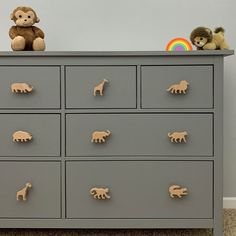 a toy monkey sitting on top of a gray dresser with many drawers and knobs