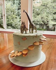 a dinosaur and giraffe on top of a cake in front of a window