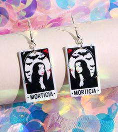 Rock these gorgeous goth girl earrings to show your dark love! Featuring Morticia Addams, Lilly Munster, Wednesday Addams, Elvira and Vampira- there's a pair for everyone! Give this spooky gift to your favorite ghouls! Earrings are printed on both sides. Gothic Earrings For Costume Party, Halloween Emo Pierced Earrings, Emo Halloween Pierced Earrings, Black Gothic Earrings For Cosplay, Black Earrings For Halloween Cosplay, Black Halloween Cosplay Earrings, Lilly Munster, Earrings Goth, Jewelry Goth