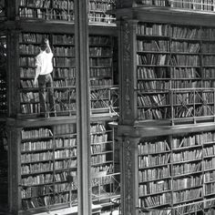 an old black and white photo of a man standing on bookshelves in a library