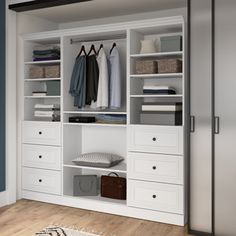 a white closet with drawers and clothes hanging on the doors, next to a rug