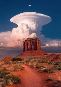 a large cloud looms in the sky over a dirt path leading to a rock formation