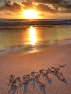 the word happy written in the sand on a beach at sunset with clouds and sun behind it