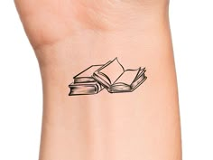 a small tattoo on the wrist of a woman's arm with an open book