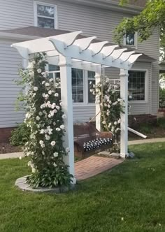 a white pergola sitting on top of a lush green field next to a house