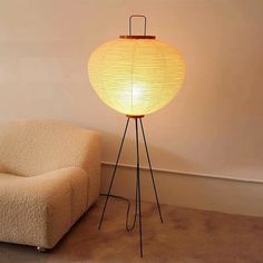 a floor lamp sitting on top of a wooden tripod next to a white chair