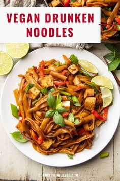 a white plate topped with noodles and veggies next to lime wedges on a wooden table