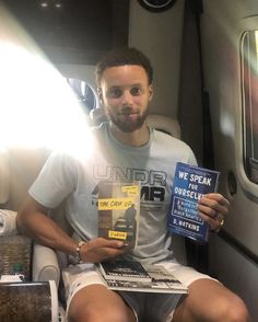 a man sitting on an airplane reading a book with his legs crossed and wearing white shorts