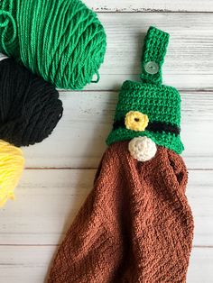 two crocheted hats are sitting next to yarn on a white wooden surface, one is green and the other is brown