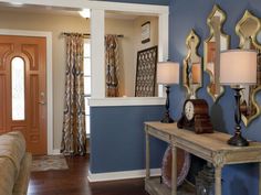 a living room with blue walls and wooden furniture in the center, along with mirrors on the wall