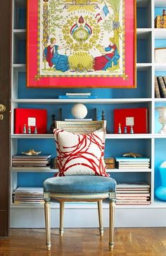 a chair in front of a book shelf with books on it and a painting hanging above