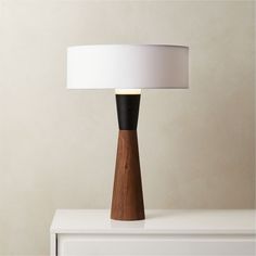 a wooden table lamp on top of a white dresser next to a beige wall and floor