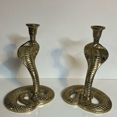 two brass cobra candlesticks sitting on top of a white table next to each other