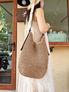 a woman carrying a straw bag in front of a storefront with a hat on her head