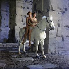 two people sitting on top of a white horse in front of an old building with columns