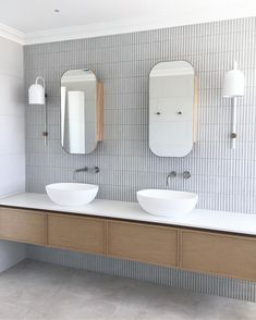 two bathroom sinks with mirrors above them in a white and grey tiled wallpapered room