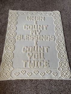 a white crocheted afghan with words written in it on the floor next to a gray carpet