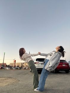 two women standing next to each other in a parking lot with their arms extended out