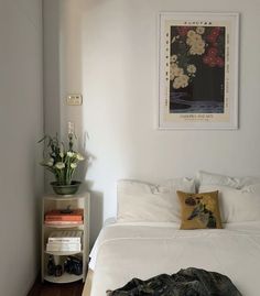 a white bed sitting in a bedroom next to a nightstand with flowers on top of it