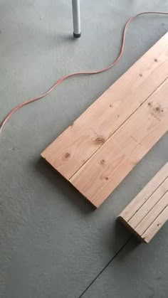 a piece of wood sitting on top of a floor next to a white pole and power cord