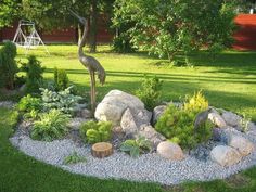 a bird statue in the middle of a garden with rocks, plants and gravel around it