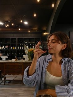 a woman sitting at a table drinking from a wine glass in front of a bar