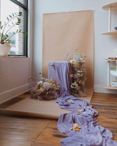 a room with flowers on the floor and a purple cloth draped over it in front of a window