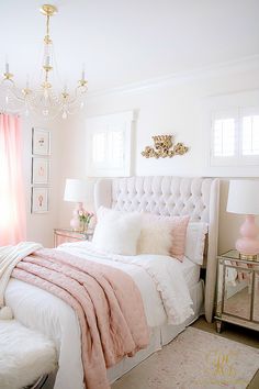 a white and pink bedroom with a chandelier, bed, pillows, rugs and lamps