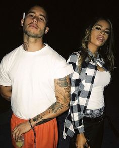 two people standing next to each other with tattoos on their arms and legs, one holding an apple