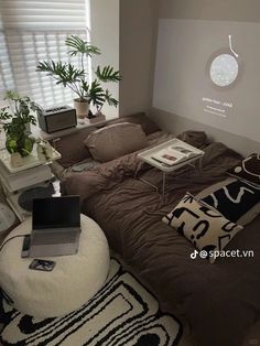 a bedroom with a bed, laptop and plants on the side table in front of it