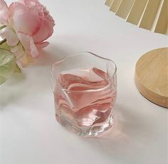 a vase with pink flowers on a white table next to a wooden stand and lamp