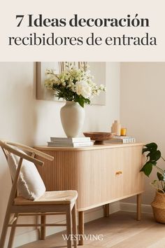 a white vase sitting on top of a wooden cabinet next to a chair and flowers