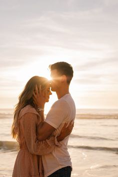 a man and woman standing next to each other on the beach with the sun behind them