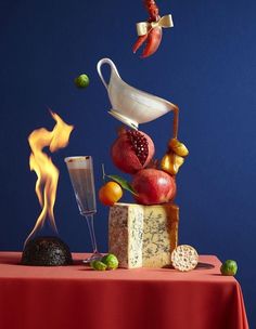 a table topped with fruit and cheese next to a glass of wine on top of a red cloth