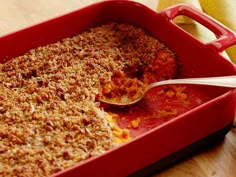 a red casserole dish with a spoon in it and some other food on the side